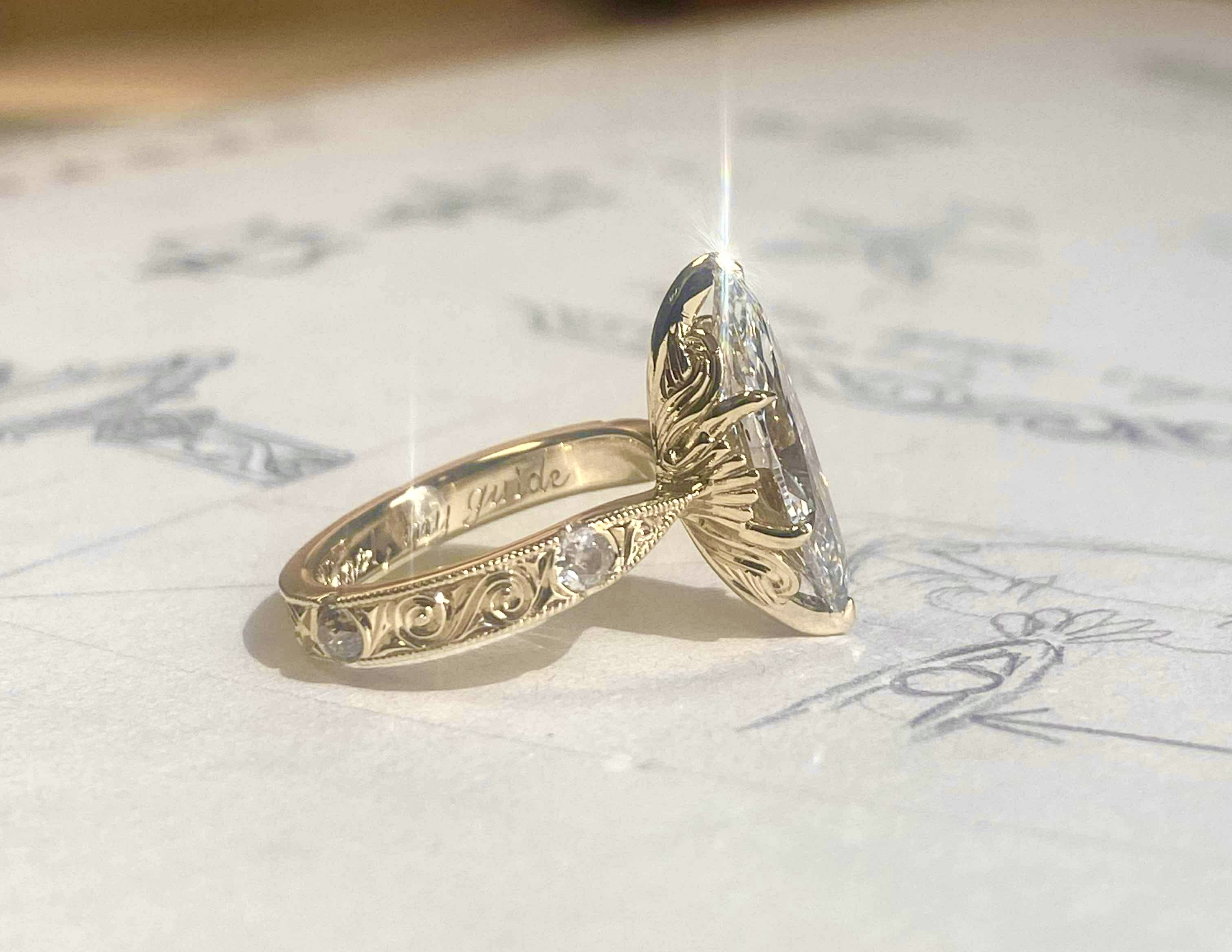 Custom hand-engraved engagement ring with aquatic theme, marquise diamond, sitting on original design sketches