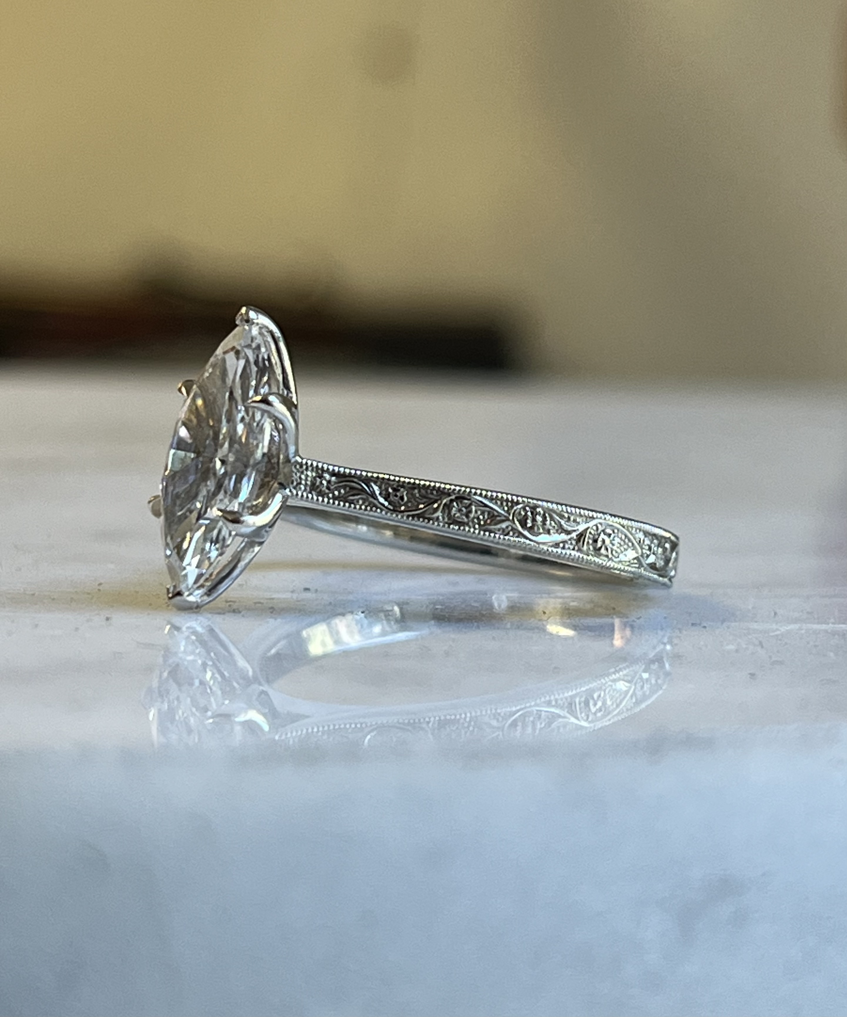 Marquise solitaire relief floral engraved white gold engagement ring pure side profile on marble showing full band engraving milgrain and flush-set accent diamonds — Bear Goldsmithing Toronto