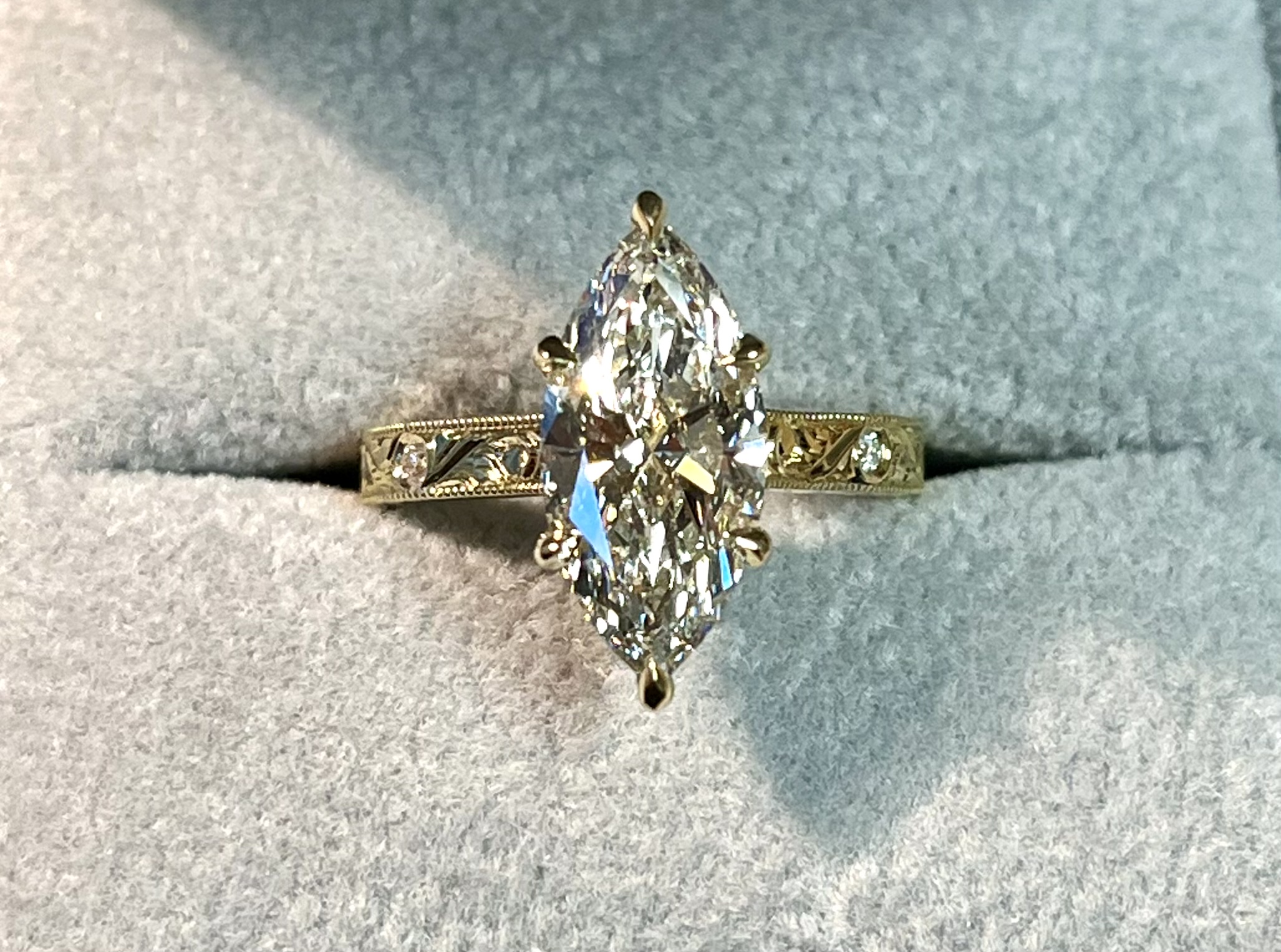 Marquise diamond solitaire yellow gold face-on in ring box showing milgrain edge flush-set accent diamonds and engraved scrollwork band — Bear Goldsmithing Toronto