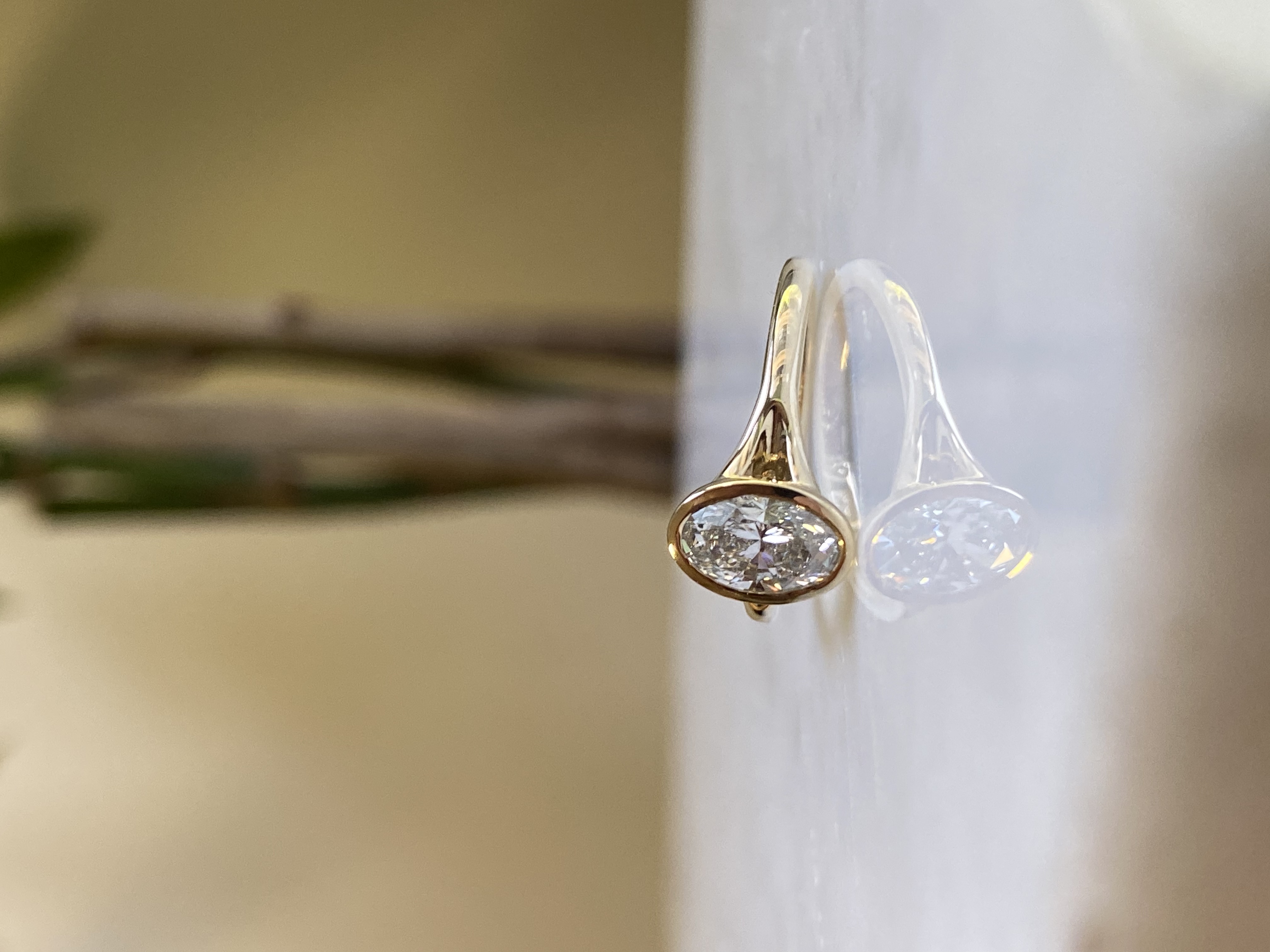 1ct oval diamond thin bezel split shank yellow gold engagement ring 3/4 angle on marble showing split shank and bezel profile — Bear Goldsmithing Toronto