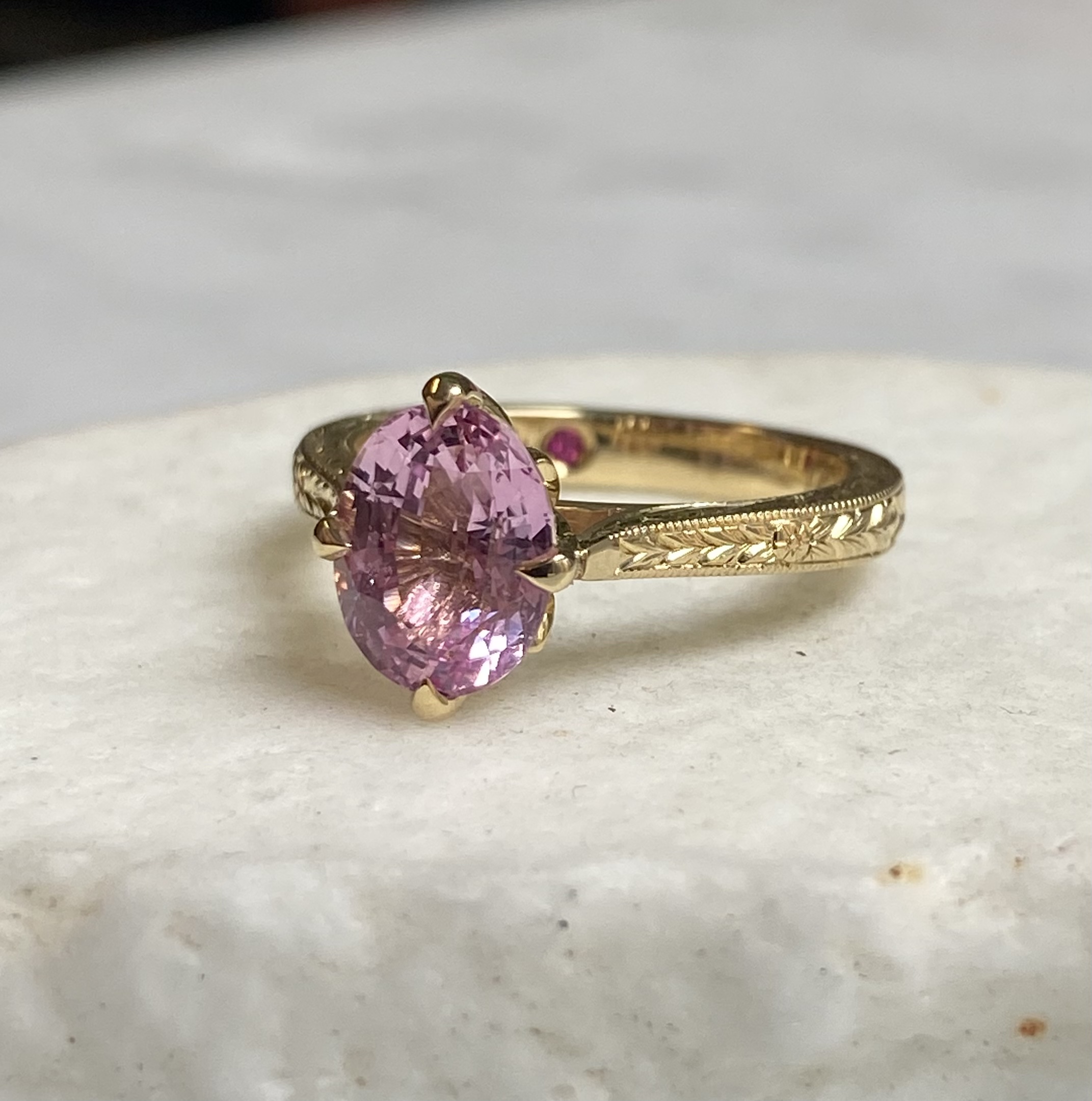 Hand-engraved wheat pattern yellow gold solitaire with oval pink sapphire leaf-cut claws and hidden pink sapphire accent — Bear Goldsmithing Toronto